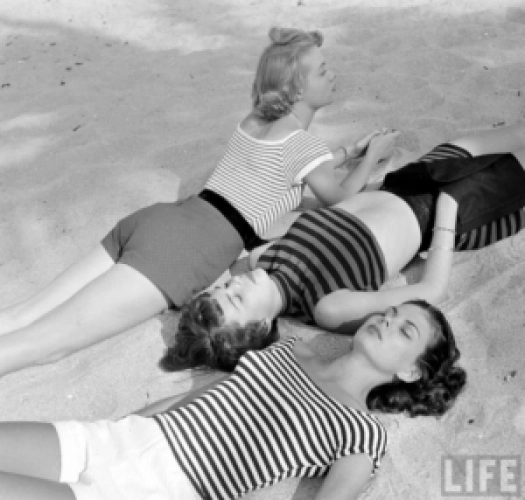 1950's summer photo of 3 young women in shorts and striped tops laying on the beach. Fun 1950s Summer Fashion