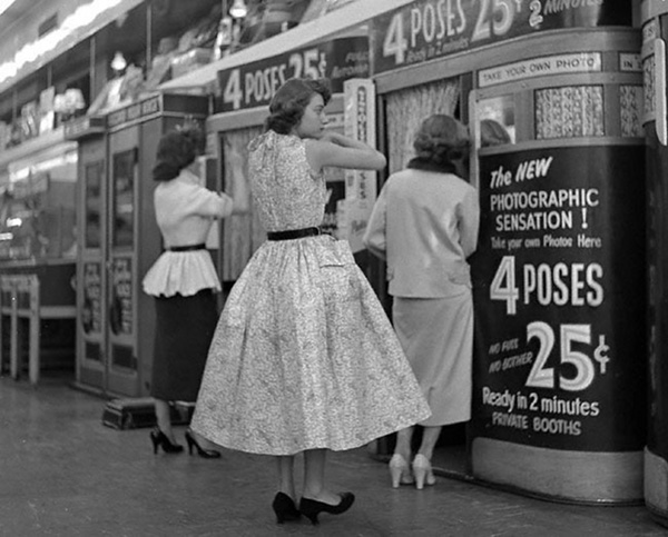 1950s vintage photo of women in 1950s fashions (1950s dress, 1940s skirts and 1950s tops) waiting to go into a photo booth in New York City.