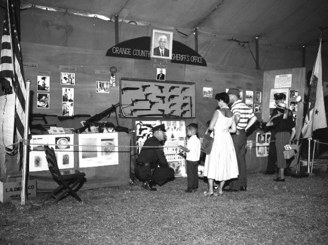 1950s vintage photo of a family in 1950s fashions at the country fair looking at a police exhibit. 