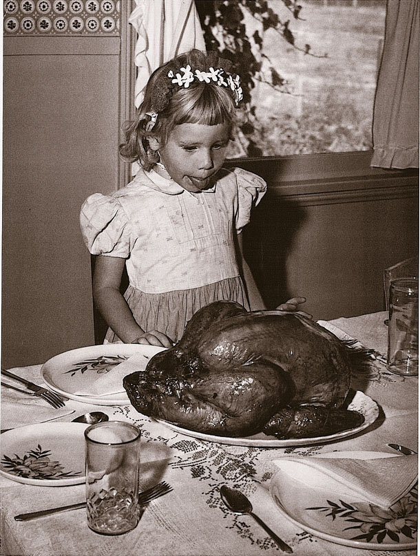 Vintage photo of a young girl standing in front of the turkey with her tongue out for Thanksgiving. 