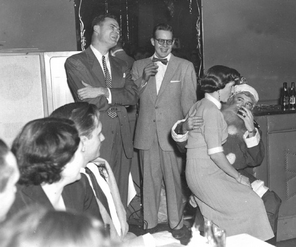 1950s vintage christmas party featuring a woman sitting on Santas lap. 