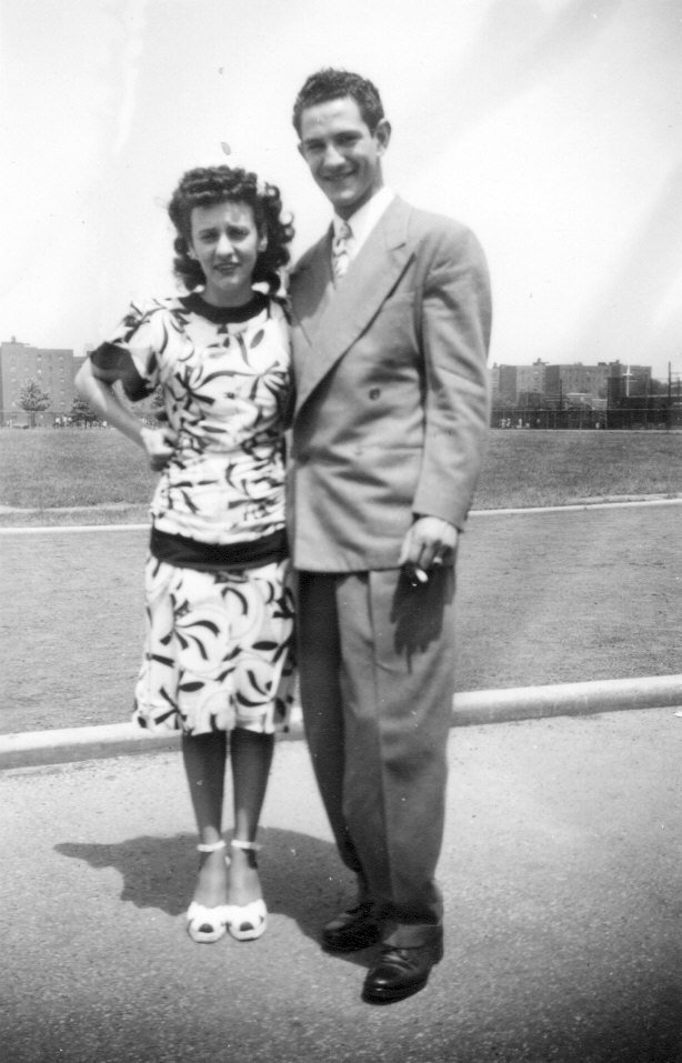 1940s vintage photo of a man and woman posing together in 1940s fashions. The woman is wearing a pretty 1940s dress and cute peep toe shoes. Our man is in a stylish suit. 