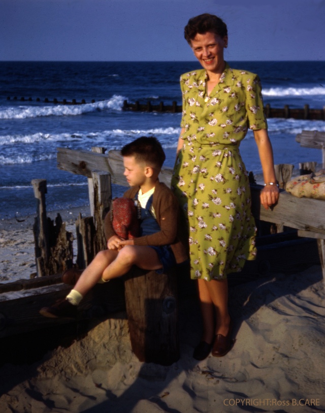 1940s vintage photo of a woman in a green floral dress posing at the ocean with a child. Lovely 1940s fashion inspiration. 