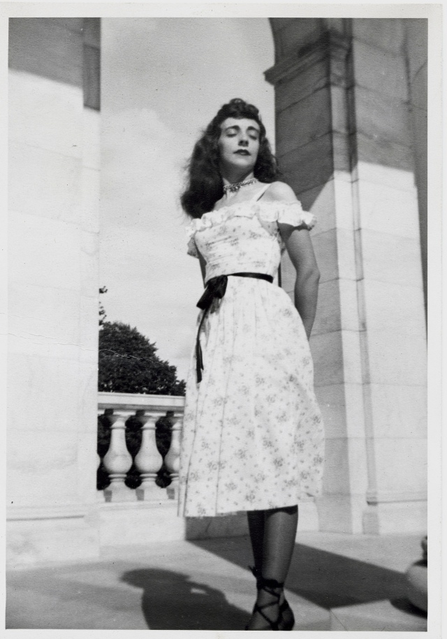 1940s vintage photo of a young woman posing for a photo in a an off the shoulder floral dress with a ribbon belt. She is wearing a choker as well. 