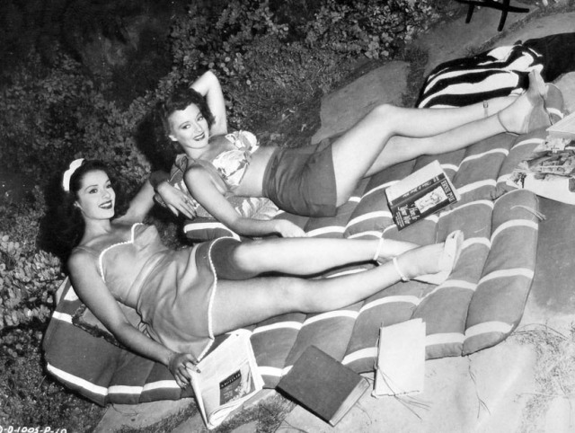 1940s vintage photo of Jinx Falkenburg and Evelyn Keyes finding a pleasant way to pass the time between their scenes in Nine Girls. They are wearing 1940s fashions - 1940s playsuit & 1940s top and shorts. 