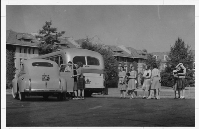 1940s vintage photo of a 1940s car and school bus with young women in 1940s fashions from Duke University waiting to take the bus. 