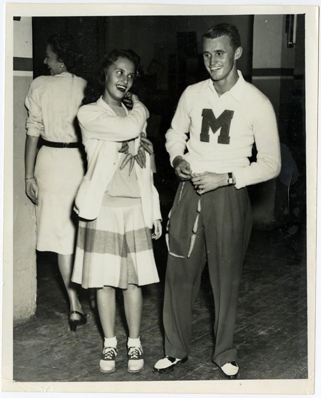 1940s vintage photo of a young man and young woman in college both wearing saddle shoes and 1940s fashion. The caption of the photo says: Campus Jane and Campus Joe, members of the University of Miami 'M' Club-1946