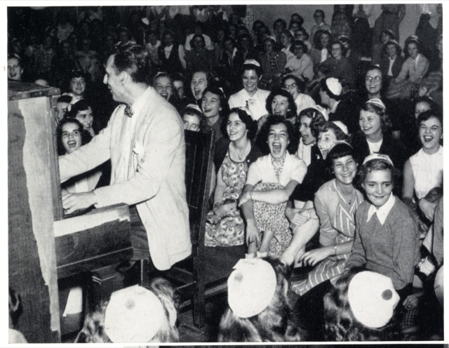 1940s vintage photo of young college students watching a band play. They are all wearing beanies as they are freshmen students. 